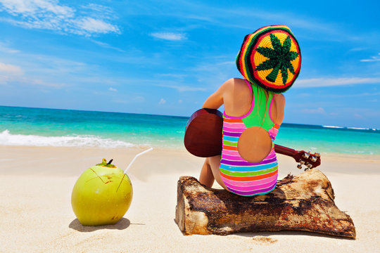 Little baby in rasta hat play reggae music on Hawaiian ukulele, enjoy relaxing on ocean beach. Kids healthy lifestyle. Family summer holiday. Activity on tropical Jamaica and Caribbean island travel.