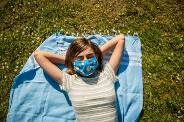 Eine Teenagerin mit selbstgenähten Mundschutz beim Sonnenbad in einem Park