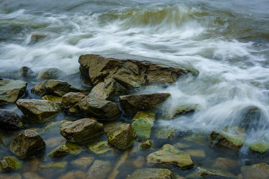 Landscape with waves crashing against the coastal stones at sunrise.