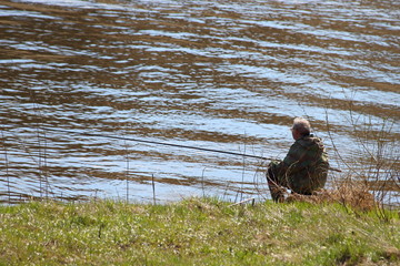 Fisherman with a fishing rod sitting on the river Bank on a spring day, calm outdoor recreation