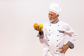 Image of senior chef holding  fruit and thinking on gray background.