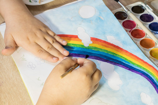 A child paints a rainbow with watercolors. Drawing a rainbow with brushes and paints in a sketchbook