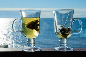 Two transparent glass cups with a bag of green leaf tea on a background of the sea.
