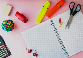 open notebook in a cage on a pink background. keyboard layout. next to office supplies. business concept for a girl or back to school
