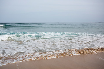 
orilla del mar con arena y olas en el fondo el horizonte entre el mar y el cielo azul.