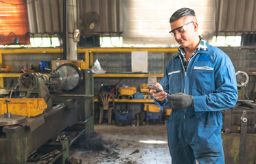 Engineers, experienced technicians Caucasian man are using mobile phone before working by controlling steel lathes, flange plates in parts production line at workplace in the industrial factory