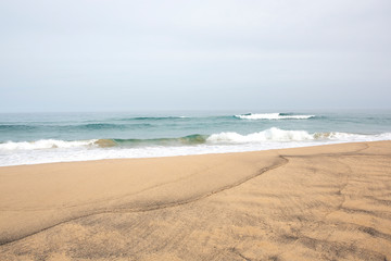 
orilla del mar con arena y olas en el fondo el horizonte entre el mar y el cielo azul.