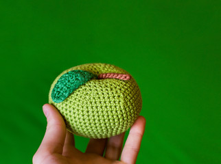 photo knitted toy apple in hand on a green background