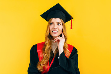 A thoughtful, graduate in a master's dress, on a yellow background. Concept of the graduation ceremony