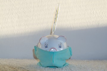 Piggy bank with the thermometer in respirator mask presenting the economics issues and financial savings during pandemic. Slovakia