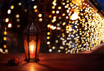 Ramadan lantern on the table. Dark background with light and bokehs. Beautiful Greeting Card with copy space for Ramadan and Muslim Holidays. An illuminated Arabic lamp. Mixed media.