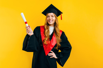 Excited beautiful graduate, with a diploma on a yellow background. Concept of the graduation...
