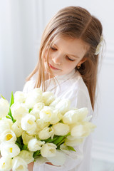 Naklejka premium Portrait of beautiful pretty girl with white flowers tulips sitting on chair, smiling. Indoor photo.