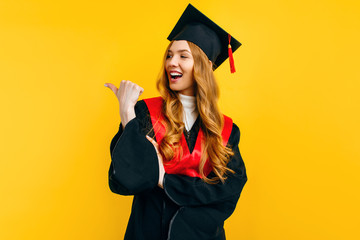 Female-a graduate of the finger pointing on copy space isolated on yellow background