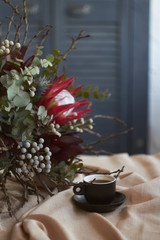 Cup of coffee and exotic bouquet without packaging stands on table with beige linen tablecloth, holiday morning concept, selective focus