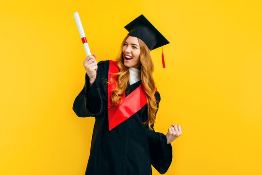 graduate girl with a diploma, shows a gesture of victory and success, on a yellow background.