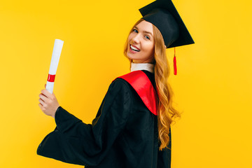 Excited beautiful graduate, with a diploma on a yellow background. Concept of the graduation...