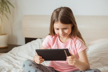 Happy teen girl watching online movie stream with digital mobile tablet and lying on bed at home in morning, video call connection, social distancing, network technology concept