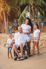 Disabled man in a wheelchair with his family on the beach.