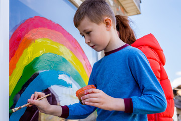 Children paint a rainbow with colorful paints on the window. This is a sign of hope and recovery from Covit-19.