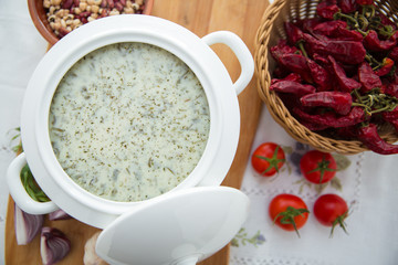 Dovga in the on wooden board . National food of azerbaijan . Creamy soup dovga . Azerbaijani Dovga soup with greens on a white bowl . Red tomato . Red Dry Pepper in Traditional Basket .