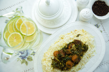 A bowl of white ceramic salt and pepper. Shah pilaf. Khan pilaf in a pita. Black pepper in a white ceramic pot . There is meat and plum chestnuts on the pilaf . Rice in a white plate. Sliced lemon .