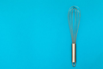 Metal whisk for whipping on a blue background.