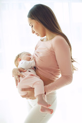 Beautiful woman breastfeeding her baby in a cozy house on the bed.