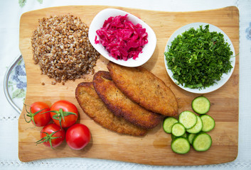 Meat cutlets, baked buckwheat on a wooden board . Red cabbage sauerkraut . Garlic, Onion, Tomatoes. Chopped coriander. Homemade cutlets with oatmeal on a table . Meat cutlets on a wooden skewer .