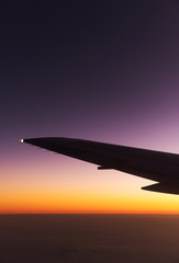 Airplane above the clouds at sunrise. Airplane wing silhouette on the background of dawn.