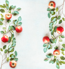 Frame made with red apples and green branches with leaves on white desk background. Top view. Flat...