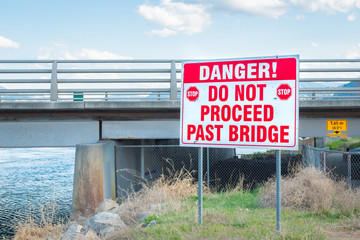 Large danger sign where river channel enters lake under bridge
