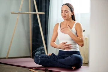 Gordijnen attractive caucasian yogi woman inhale the fragrance of aroma sticks, meditate at home, sitting on the floor, relax © alfa27