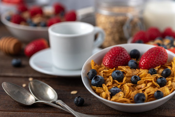 Cornflakes with blueberries and raspberries in white bowl on dark wooden desk.