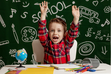 Emotional school boy sitting on the desk with many school supplies. First day of school. Kid boy from primary school. Back to school. Child from elementary school.