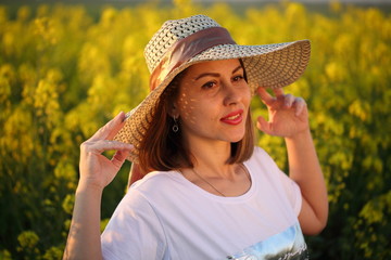 Beautiful girl in a straw hat walks in a field at sunset