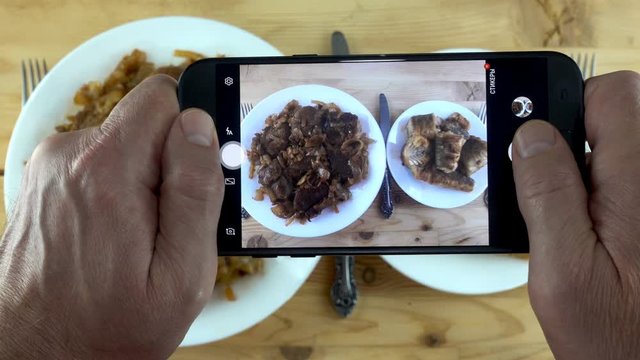 Male hands with smartphone taking pictures of dishes with fried meat and fish in 4K. Dishes with food on a wooden table