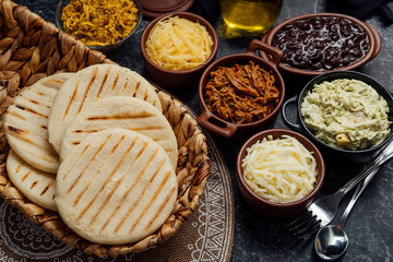 Latin arepas with various ingredients around such as meat, chicken, cheese, black beans and queen pepeada