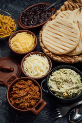 Latin arepas with various ingredients around such as meat, chicken, cheese, black beans and queen pepeada