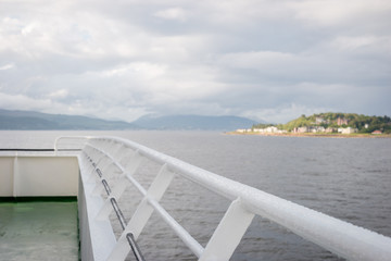 The wet rail of a passenger and car ferry showing cloud-covered islands in the UK