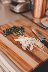 Sliced yellow white onion and herbs on cutting board. Chefs knife. Professional japanese knife. Lifestyle kitchen. Cooking process. Prepare food for dinner or lunch. Wooden board. Ready to cook. Saute