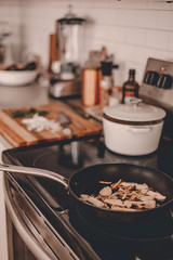 Cooking process on the kitchen. Sauteed mushrooms in frying pan. Cook dinner or lunch. Lifestyle kitchen. White cabinets. Stove top. Pro chef in the kitchen. Cooking tricks. Wild mushrooms.