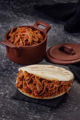Arepa stuffed with shredded meat on a dark background. (Arepa con carne mechada)