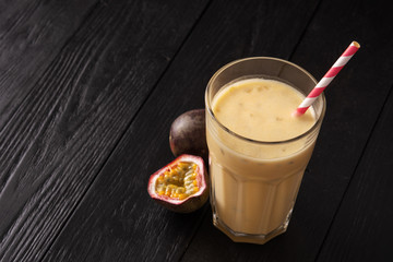 Fruit protein shake on a black wooden background. Fresh milkshake with passion fruit. A glass of protein shake.
