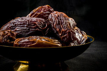 Big luxury dried date fruit in bowls on the dark surface, kurma ramadan kareem concept, close up.