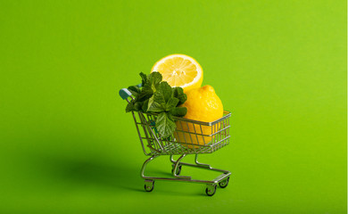 Lemons and mint in a small toy cart on a green background. online shop delivery concept