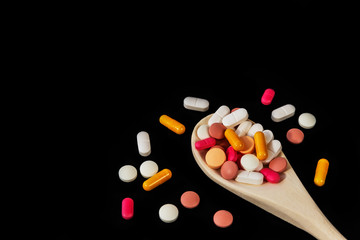 Mixed medicine pills, tablets and capsules on wooden spoon on a dark background. Many different pills and capsules. Closeup, close-up