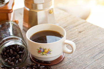 A cup of hot espresso coffee mugs and roasted coffee beans with moka pot placed on wooden floor background,coffee morning,selective focus