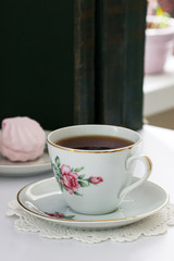 Tea in a vintage cup, marshmallows on a vintage saucer and old books on a light background.