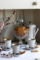 Coffee served with shortbread cookies and sweets on the background of flowering branches and an old cupboard.